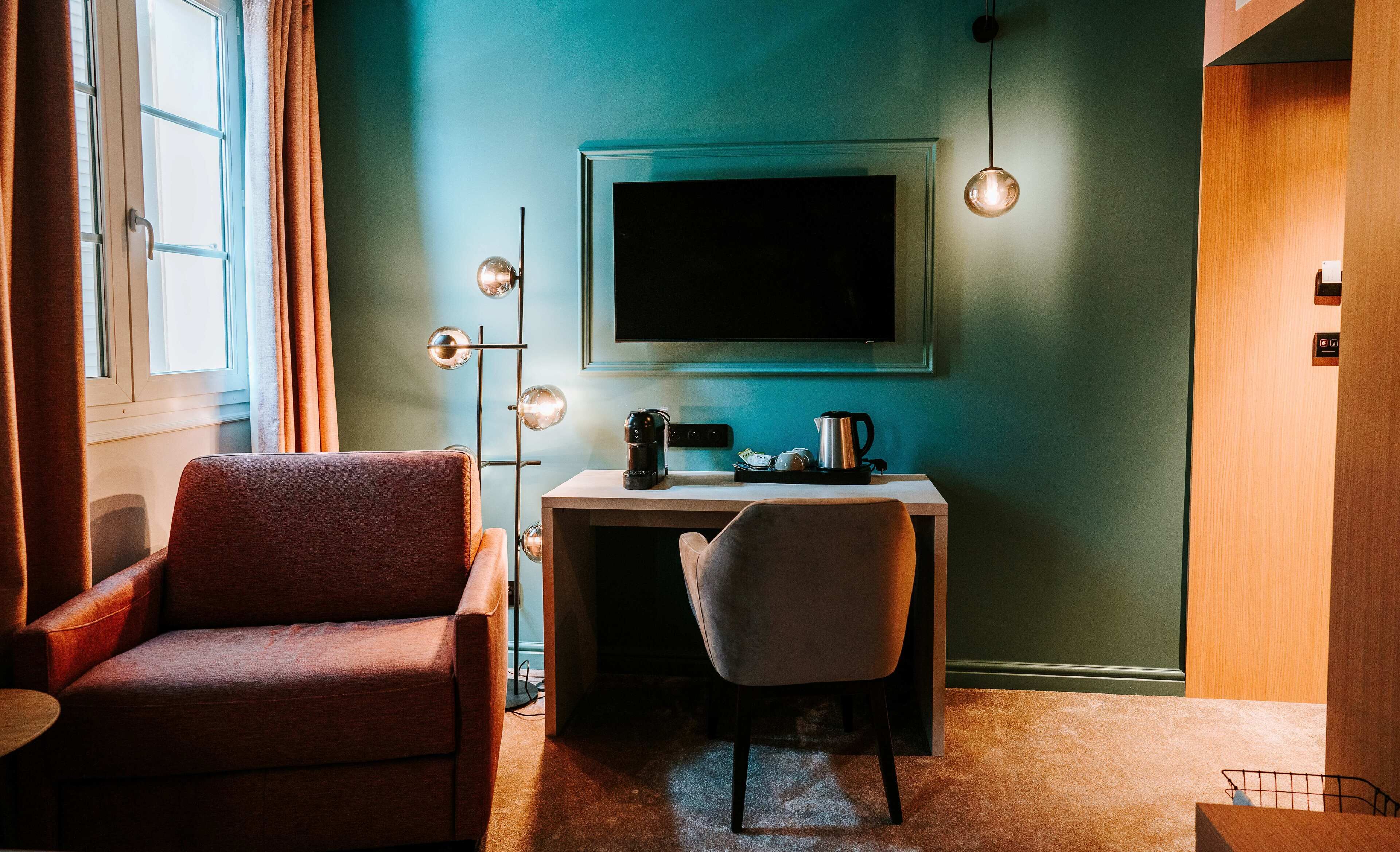 A room with a desk, a chair, a sofa, a TV, and a floor lamp.