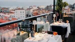 A dining table set with a bottle, glasses, and a vase of flowers, overlooking a cityscape. - Hôtel Fesch & Spa (Ajaccio)