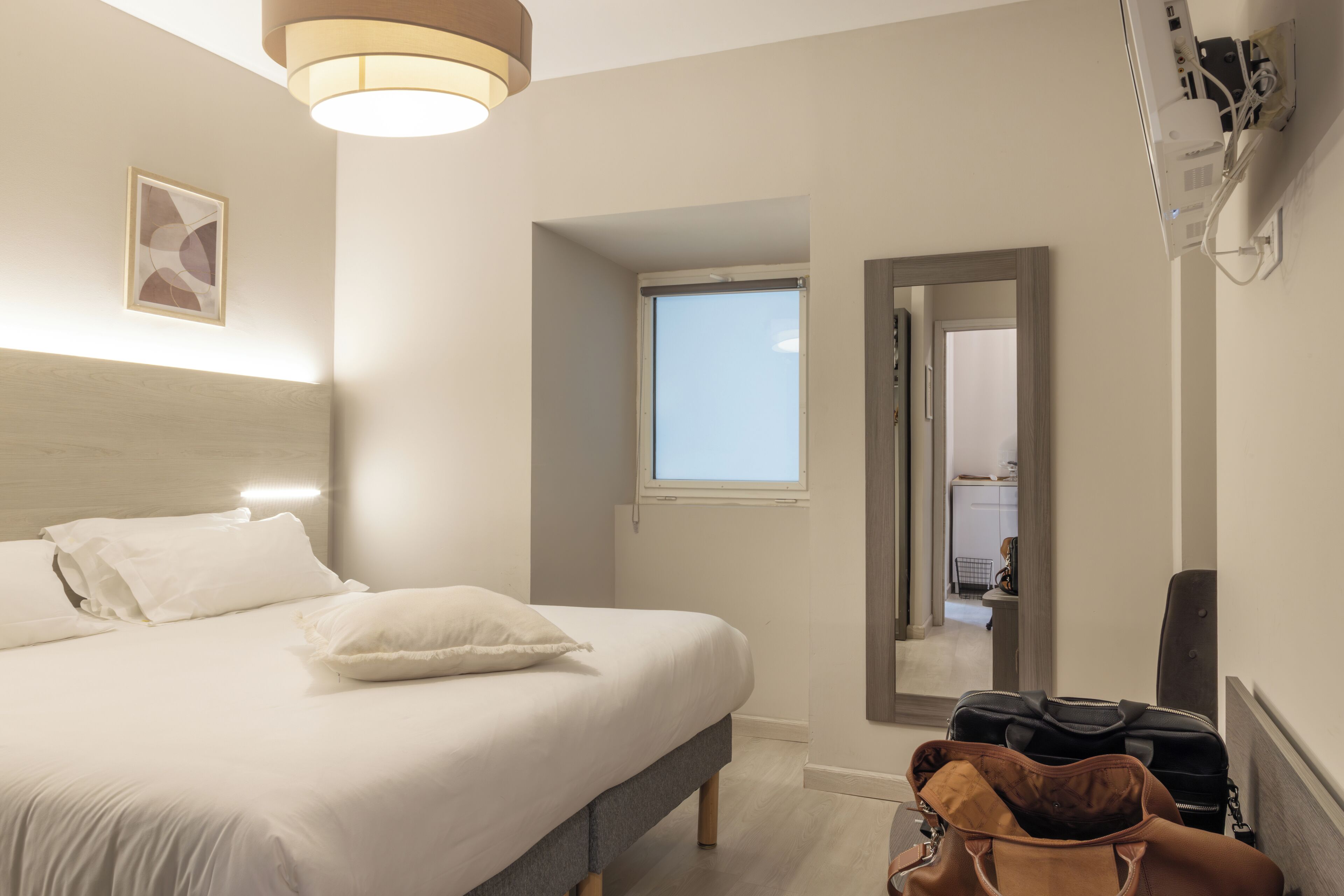 A hotel room with a bed, a window, a door, and a wall-mounted air conditioner.