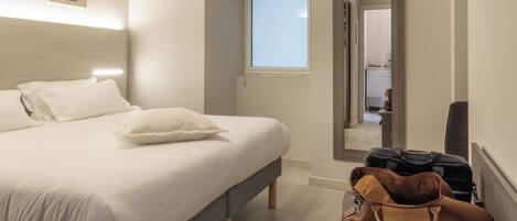 A hotel room with a bed, a window, a door, and a wall-mounted air conditioner.
