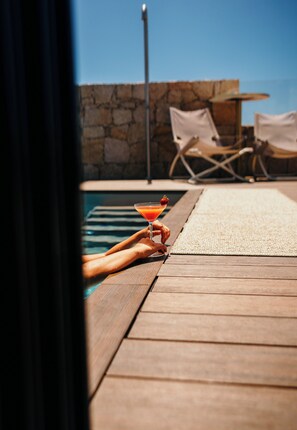 A wooden deck with a pool, lounge chairs, and a drink.