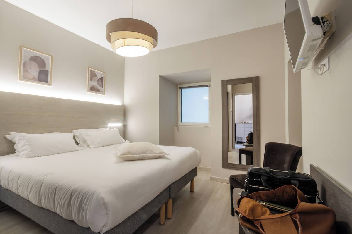 A hotel room with a bed, a chair, a desk, and a suitcase.