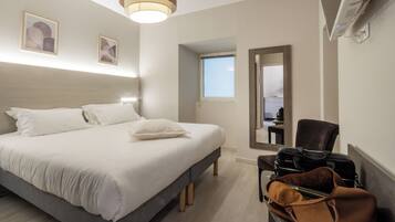 Una habitación de hotel con una cama, una silla, un escritorio y una maleta.