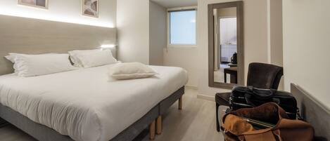 A hotel room with a bed, a chair, a desk, and a suitcase.