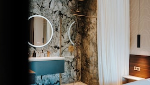 A modern bathroom with a marble wall, a sink with a gold faucet, and a shower with a glass door. - Hôtel Fesch & Spa (Ajaccio)