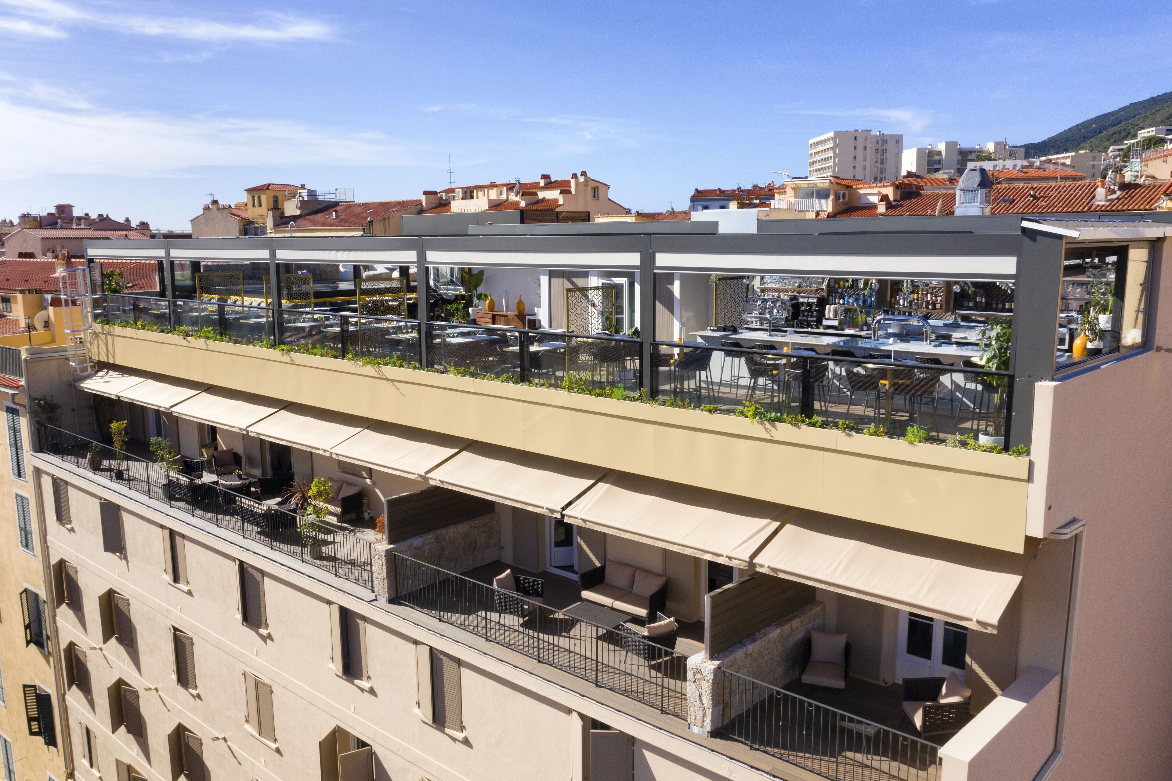 A multi-story building with outdoor seating areas on balconies, featuring railings and potted plants.