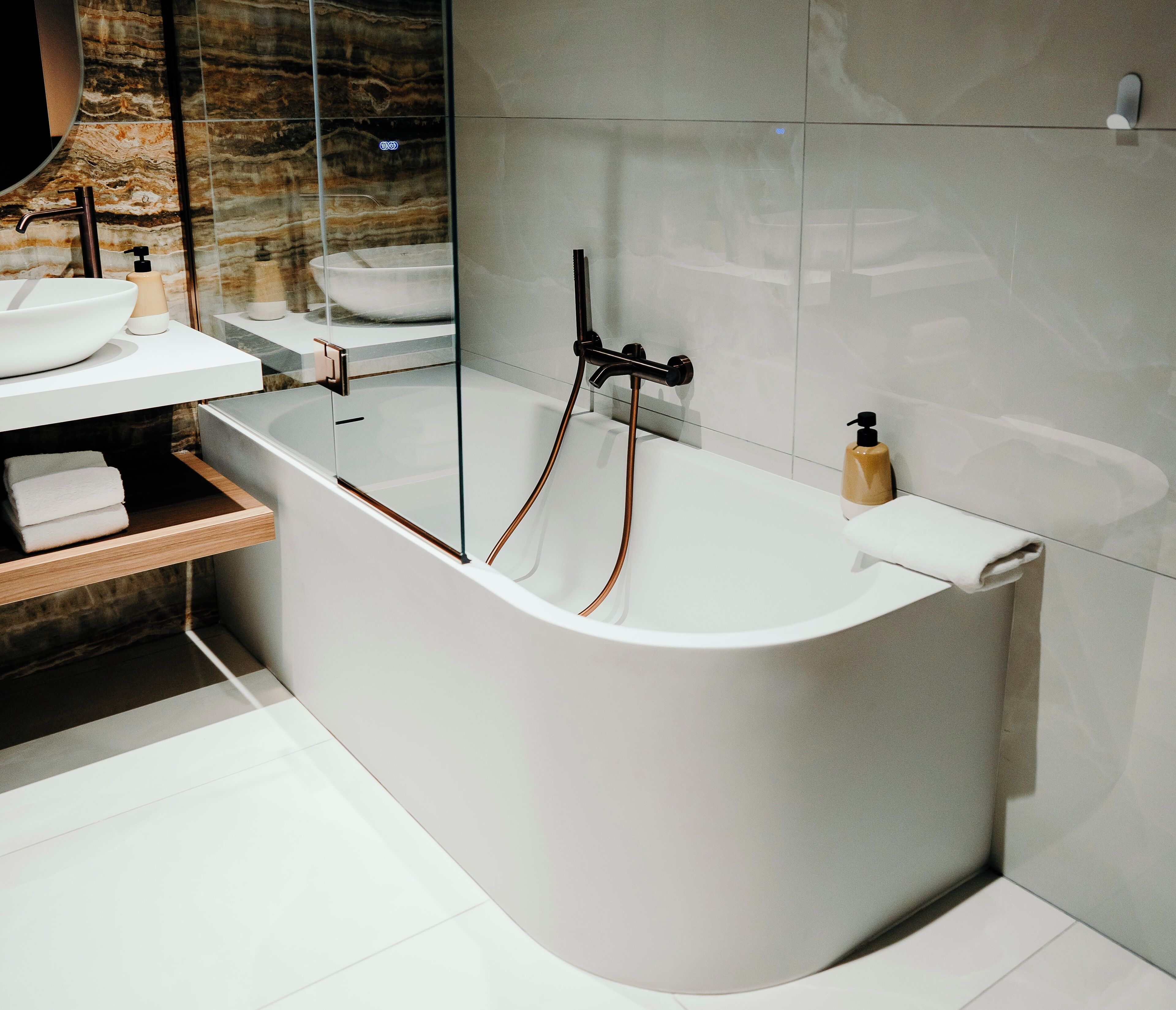 A modern bathroom with a freestanding bathtub, a glass-enclosed vanity, and a marble backsplash.