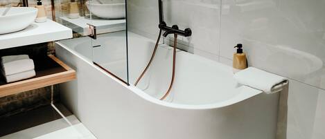 A modern bathroom with a freestanding bathtub, a glass-enclosed vanity, and a marble backsplash.