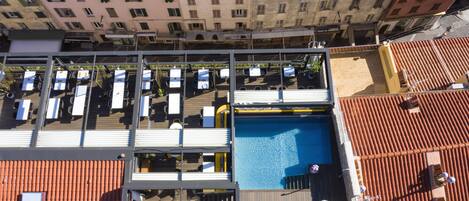 A rooftop pool area with lounge chairs, a pool, and a view of surrounding buildings.