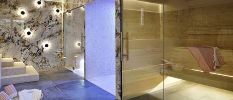 Een moderne spa met een glazen douche, marmeren wanden en een zithoek met handdoeken.