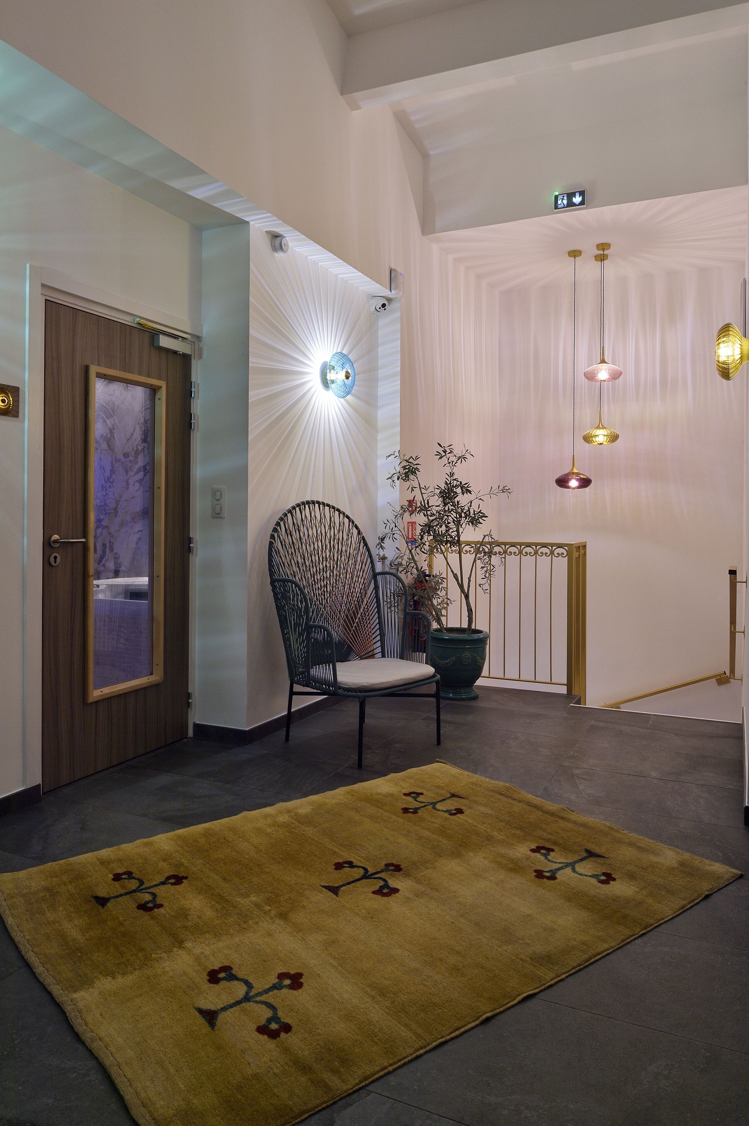 A hallway with a wooden door, a chair, a potted plant, a decorative wall, and a floor lamp.