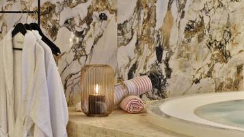 Une salle de bain avec un mur en marbre, une baignoire, des serviettes et une bougie.