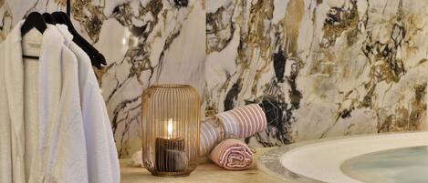 A bathroom with a marble wall, a bathtub, towels, and a candle.