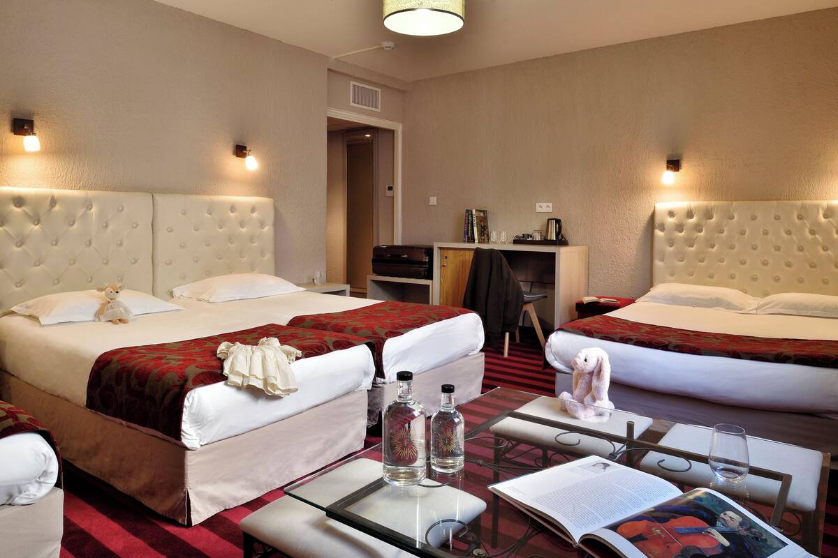 A hotel room with two beds, a desk, a chair, and a table with a magazine and glasses.