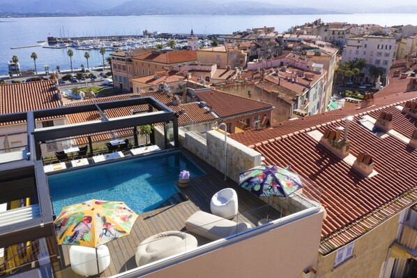 A rooftop pool area with lounge chairs and umbrellas, overlooking a marina and historic buildings.
