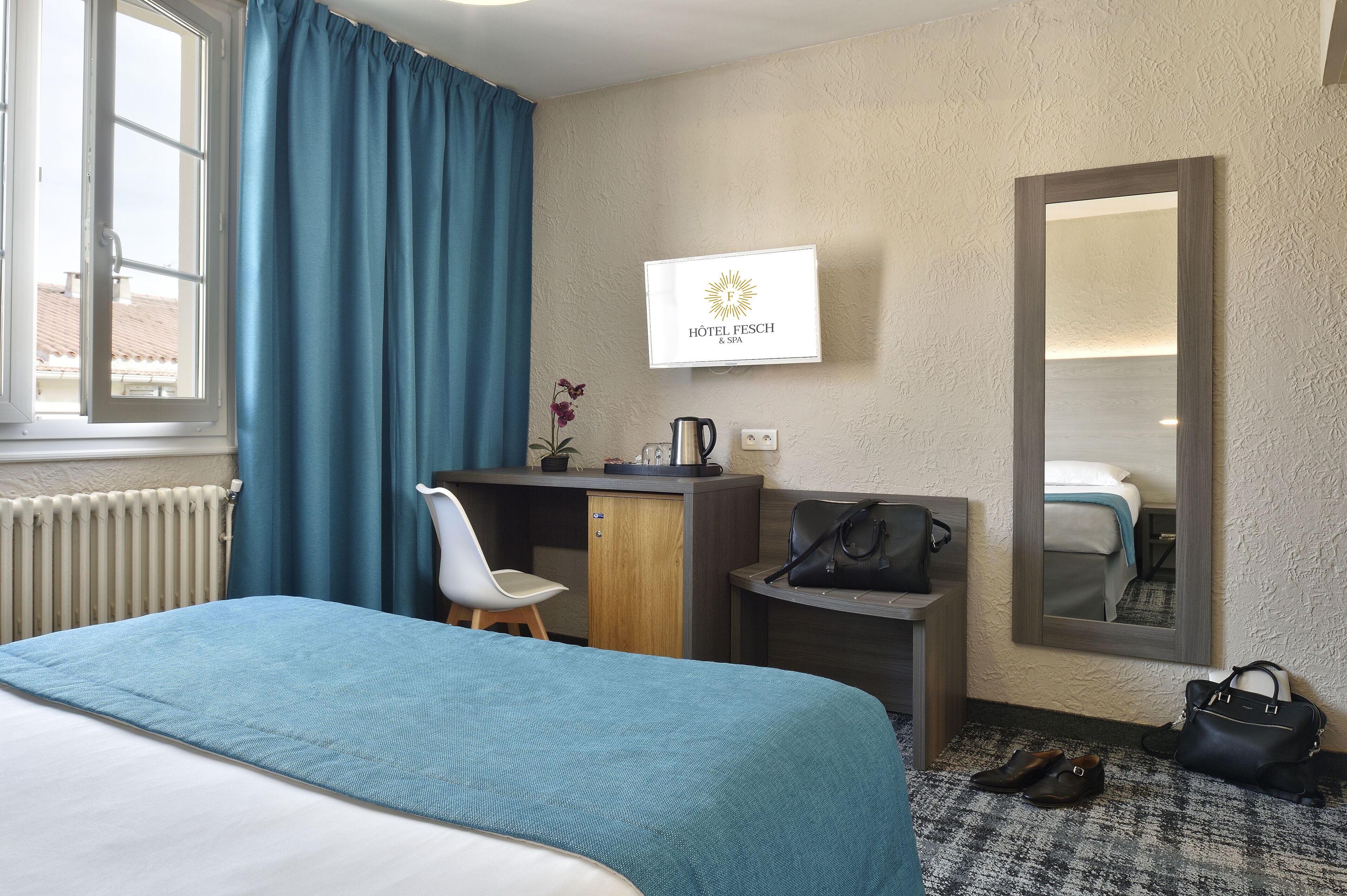 Une chambre d’hôtel équipée d’un lit, d’un bureau, d’une chaise, d’un miroir, d’une télévision et d’un radiateur.