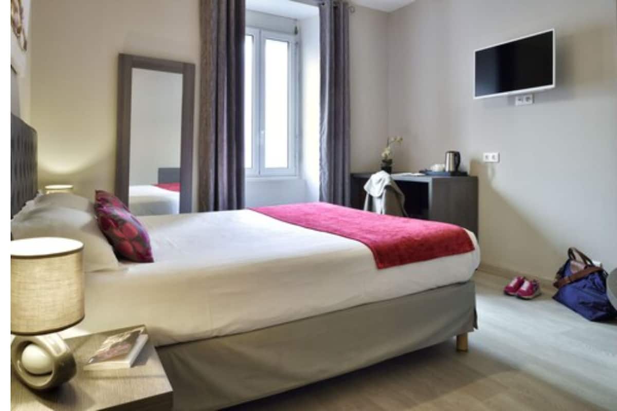 A hotel room with a bed, a desk, a chair, a TV, and a window.