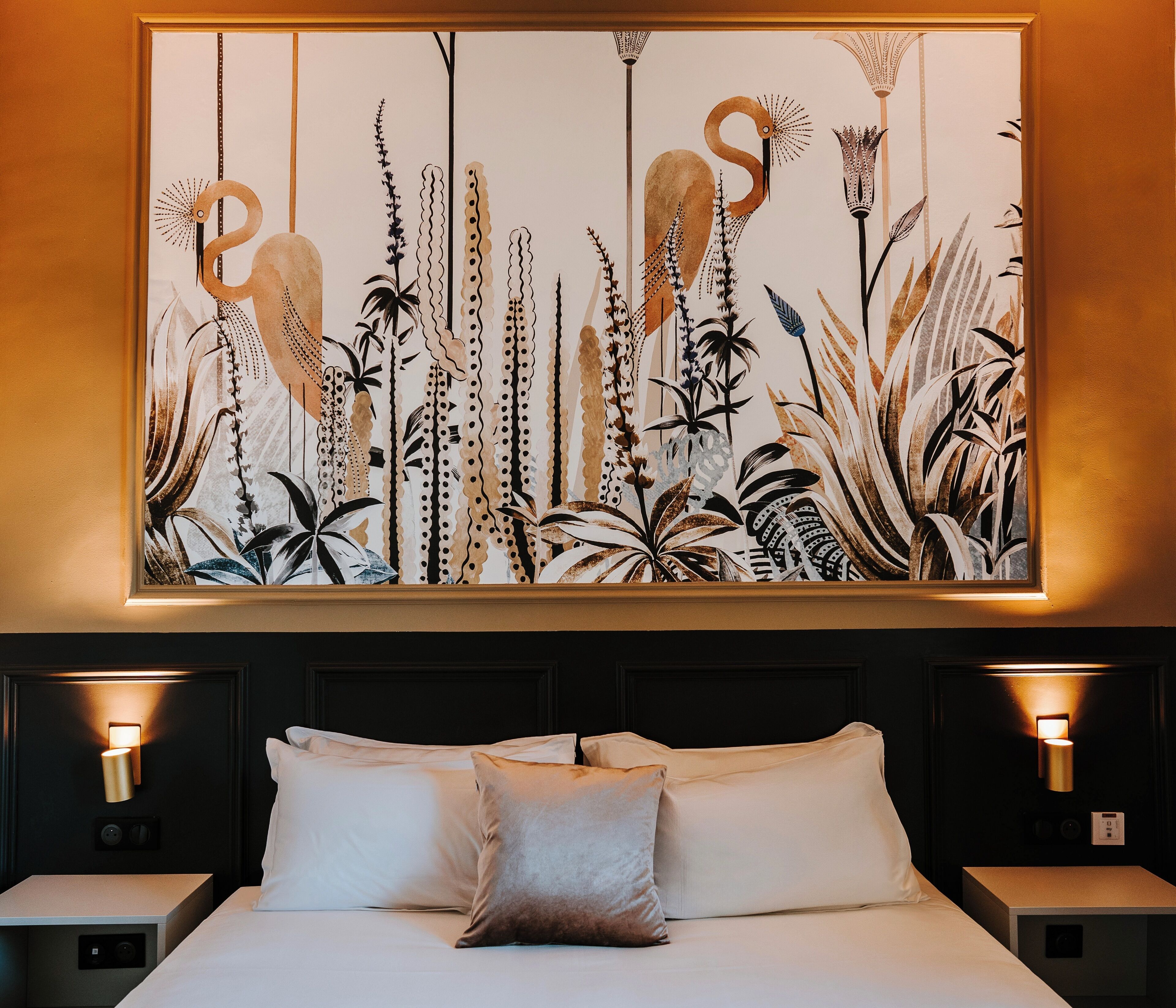 A bed with white linens, two bedside tables, and a wall-mounted artwork depicting stylized birds and plants.