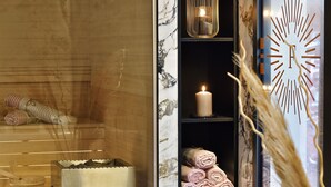 Uma área de spa com uma banheira de madeira, um recipiente de metal e toalhas enroladas em prateleiras.