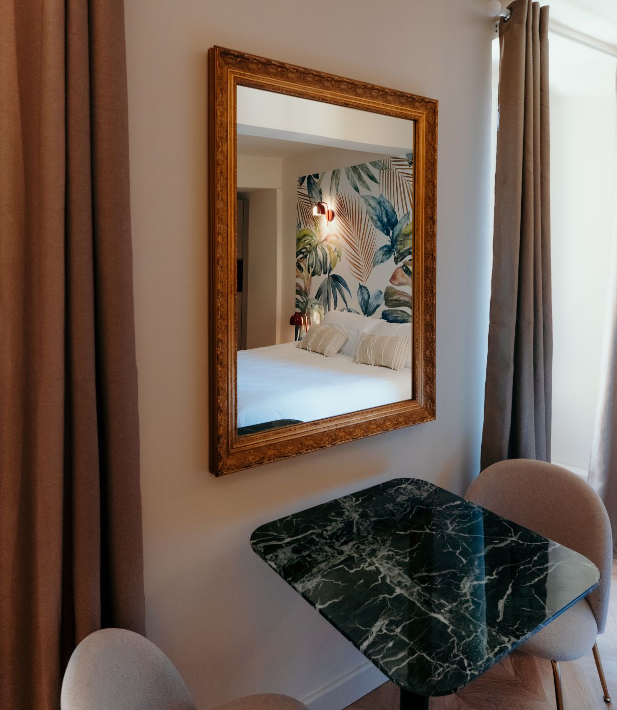 Ein Hotelzimmer mit einem Bett, einem Marmortisch, zwei Stühlen und einem großen Spiegel an der Wand.