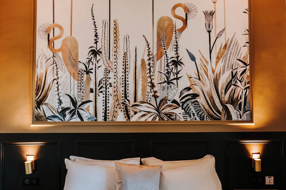 A hotel room with a large wall mural of birds and plants, a bed with white linens, and bedside lamps.