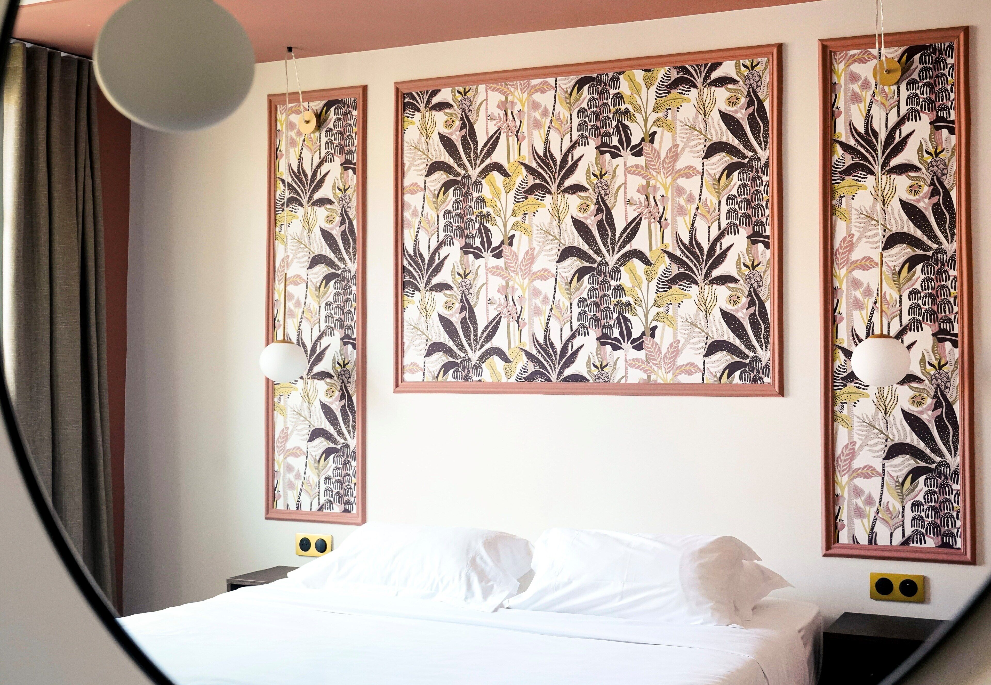 A hotel room with a bed, a nightstand, and three framed floral artworks on the wall.