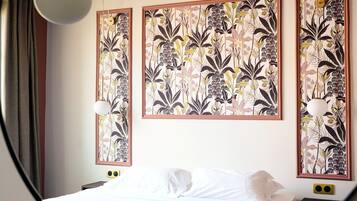 A hotel room with a bed, a nightstand, and three framed floral artworks on the wall.