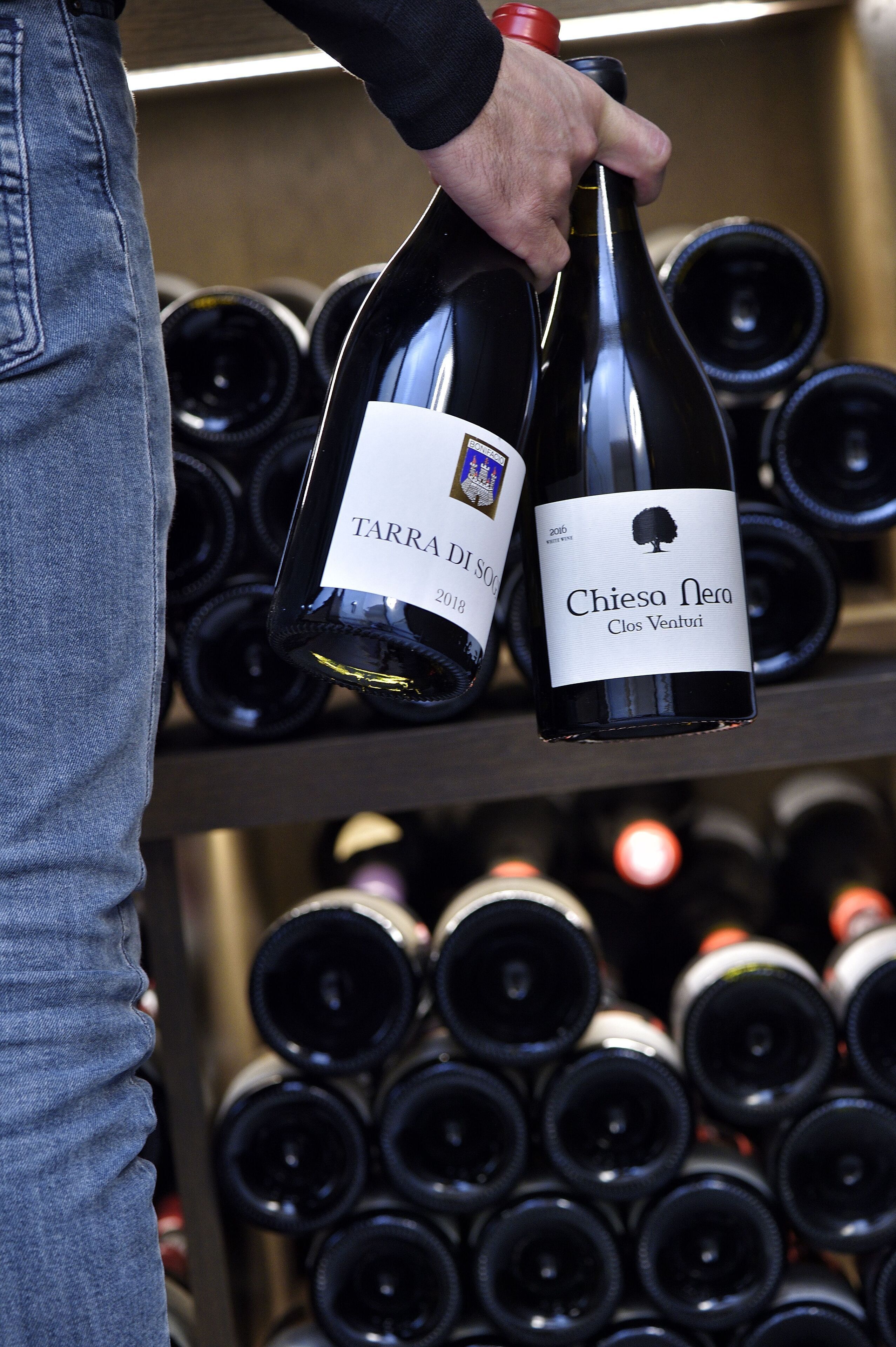 A person holding two wine bottles, one labeled 'Tarra Di Sorci' and the other 'Chiesa Nera'.