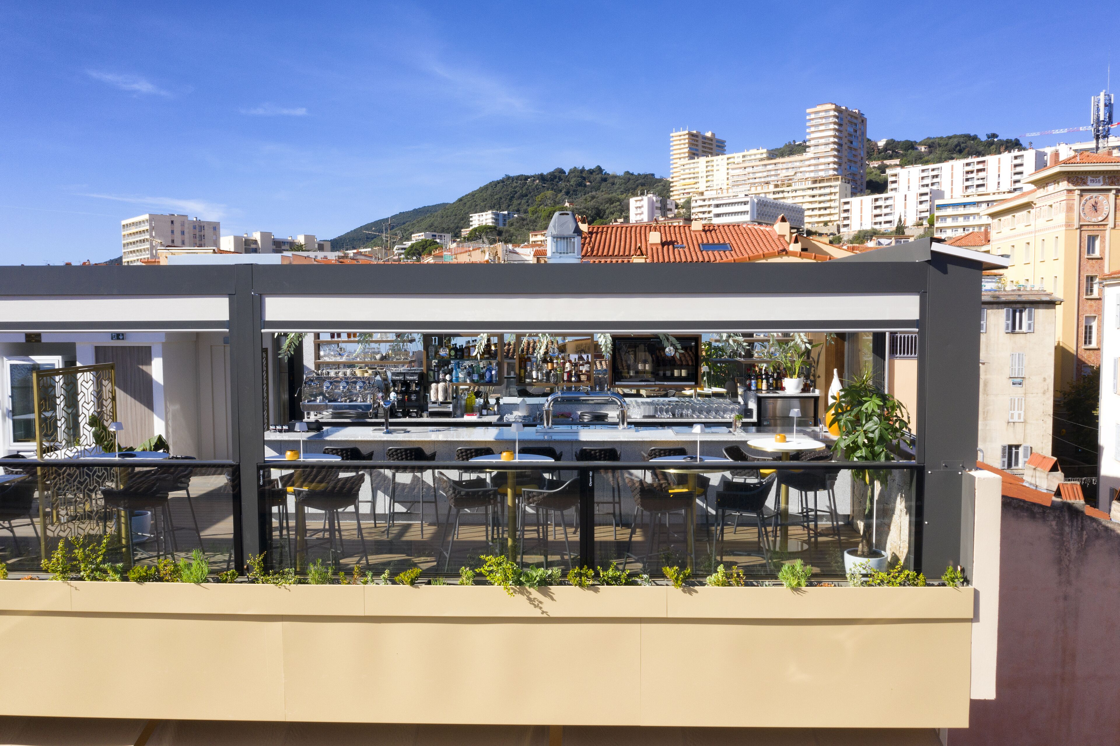 A rooftop bar with outdoor seating and a view of the cityscape.