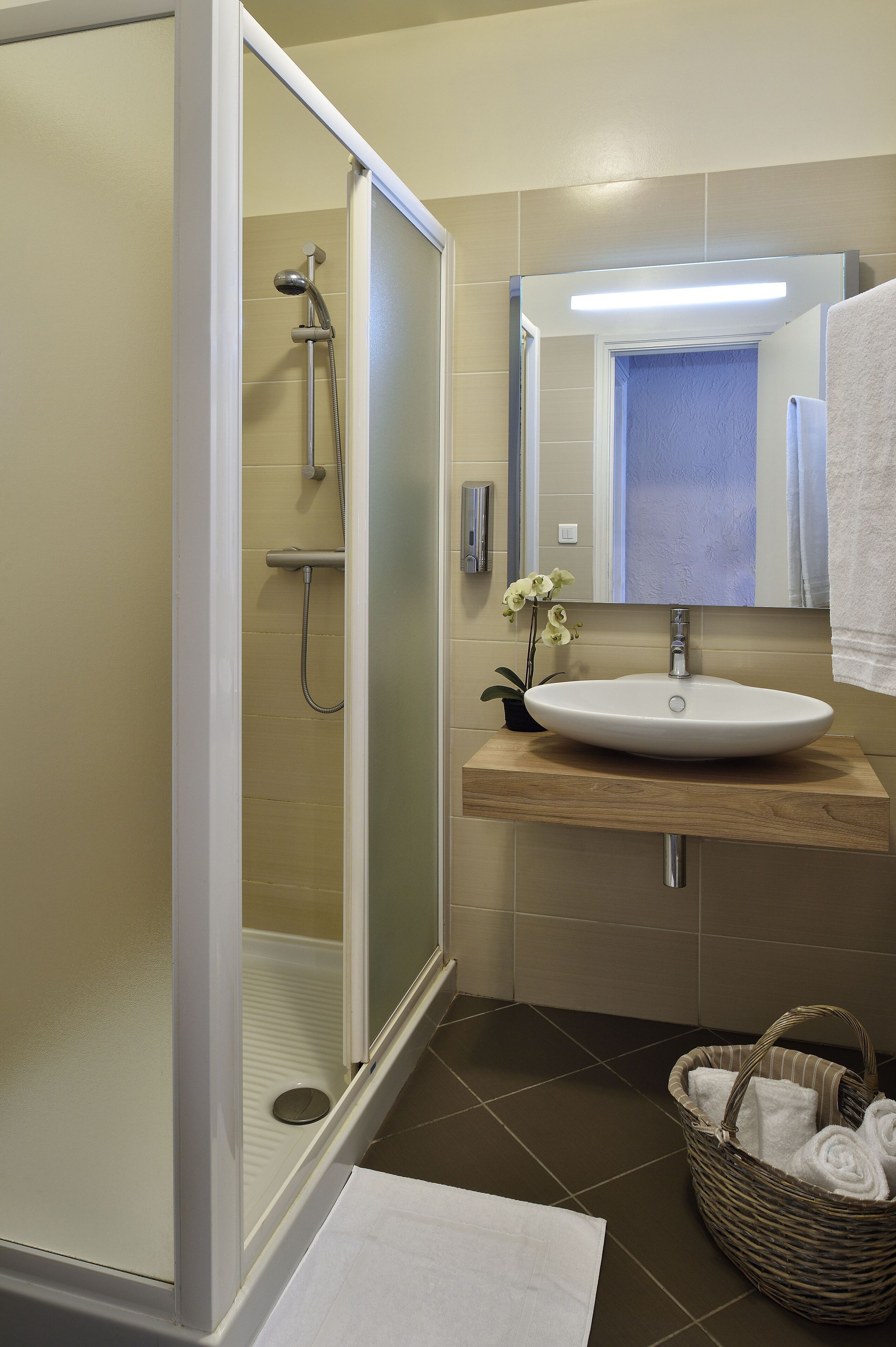 Une salle de bain avec une douche à parois de verre, un lavabo avec un miroir au-dessus et un panier en osier contenant des serviettes.