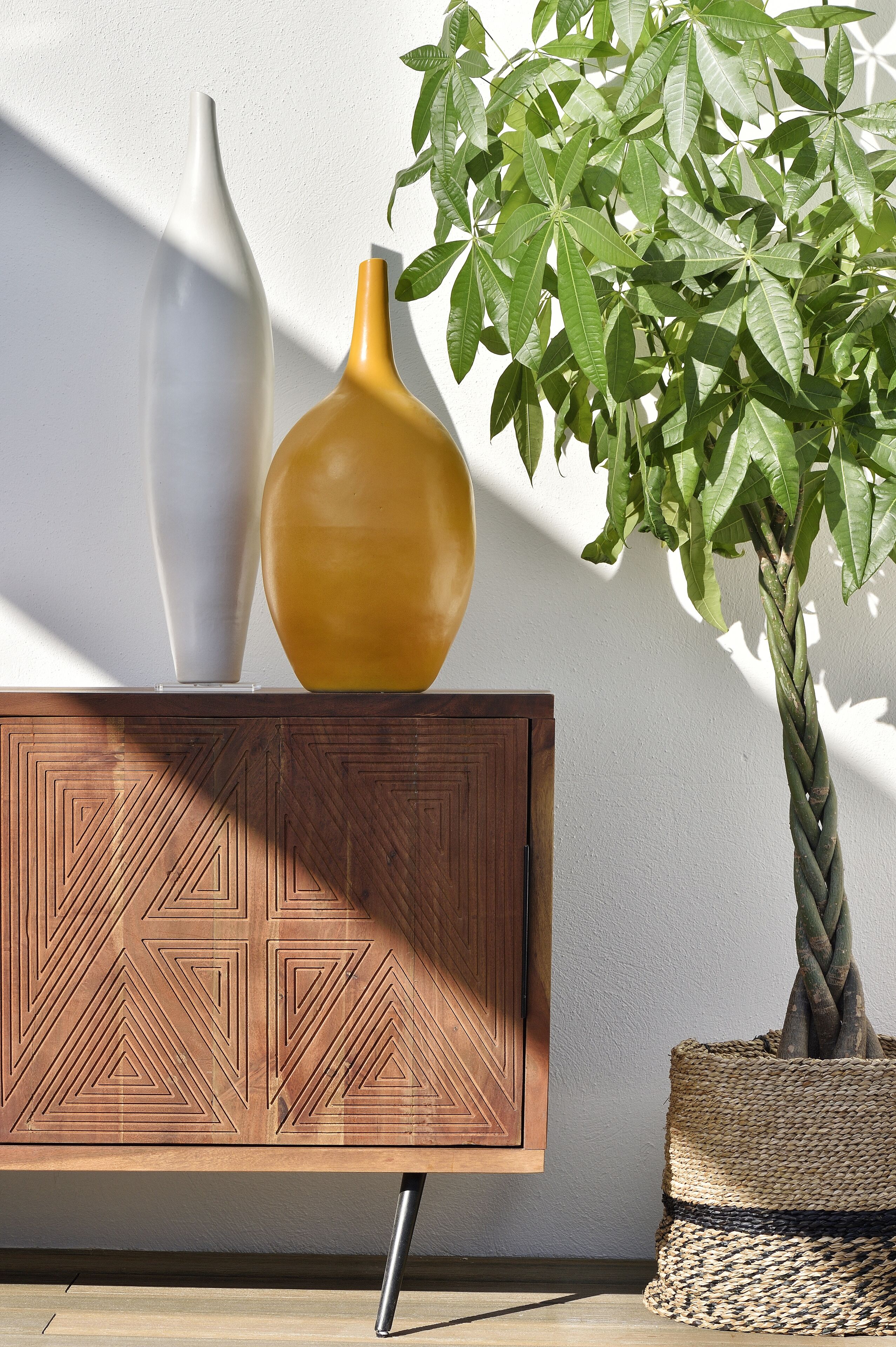 Un meuble en bois orné de motifs géométriques, deux vases et une plante en pot aux larges feuilles.