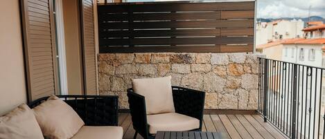 A balcony with outdoor furniture, a stone wall, and a view of buildings in the background.