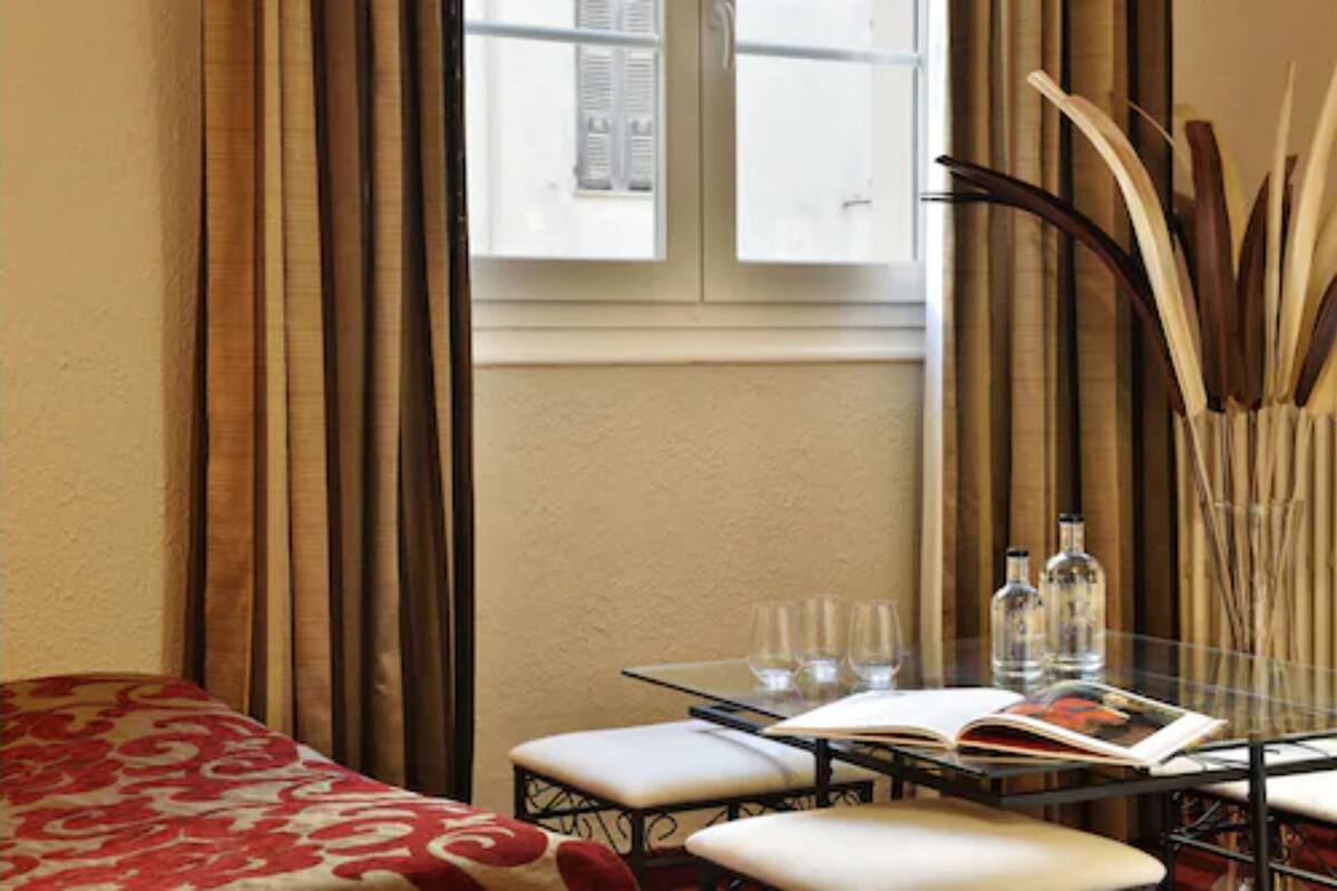 A room with a bed, a table with a book, glasses, and bottles.
