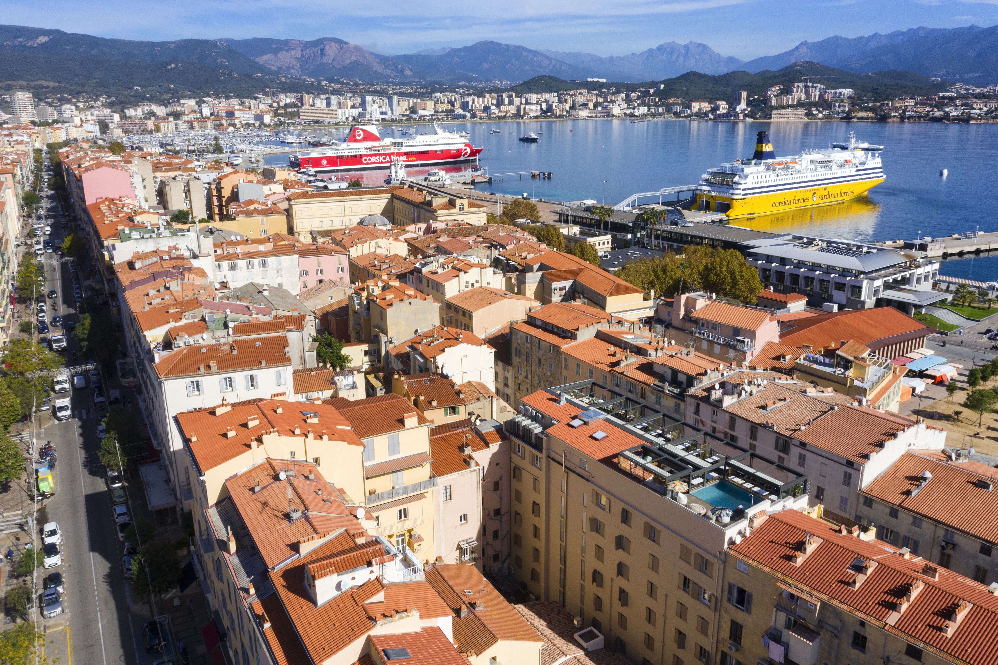 A coastal cityscape with a prominent marina, including a large cruise ship and a smaller ferry.