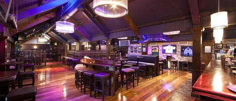 A spacious bar area with wooden flooring and multiple seating arrangements, including bar stools and high tables.