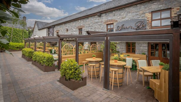 A rustic stone building with a bar named "Annal's Bar" established in 1752. It features outdoor seating with wooden tables and chairs, surrounded by planters and a brick pathway. - The Court Yard Hotel (Leixlip)
