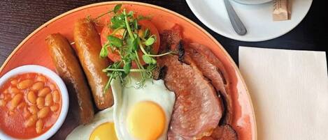 Un plato de desayuno con huevos, salchichas, tocino, champiñones, frijoles y una taza de café.