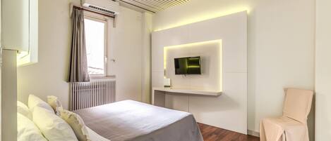 Quarto moderno com cama, televisão na parede, uma cadeira e janela com cortinas.
