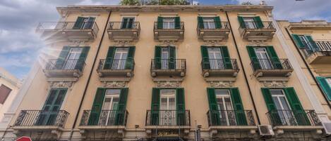 A multi-story building with a traditional architectural style, featuring balconies with green shutters and ornate railings.