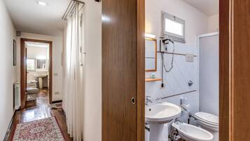 A bathroom with a wooden door, white sink, and two toilets.