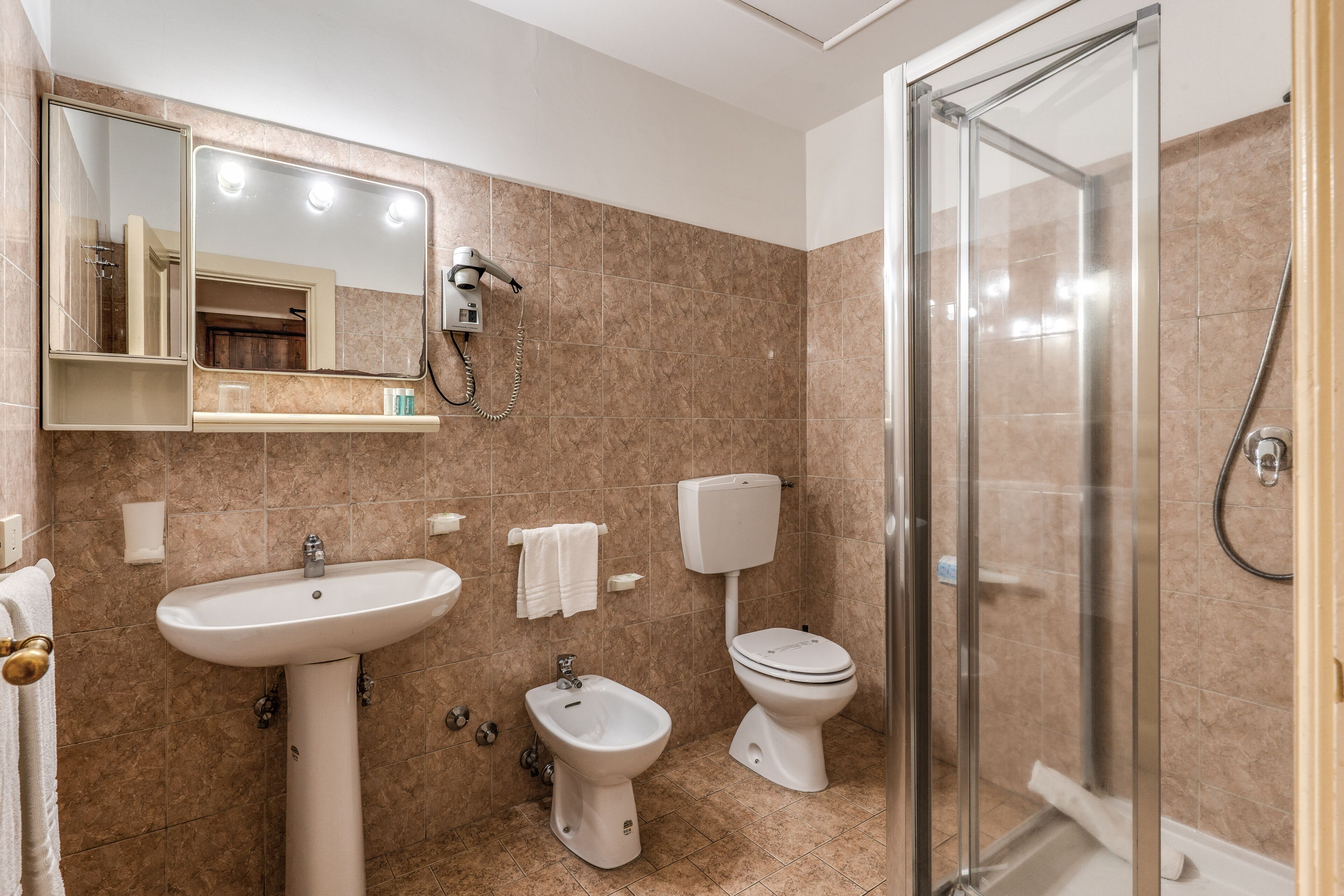 A bathroom with a sink, bidet, toilet, and a glass-enclosed shower area.