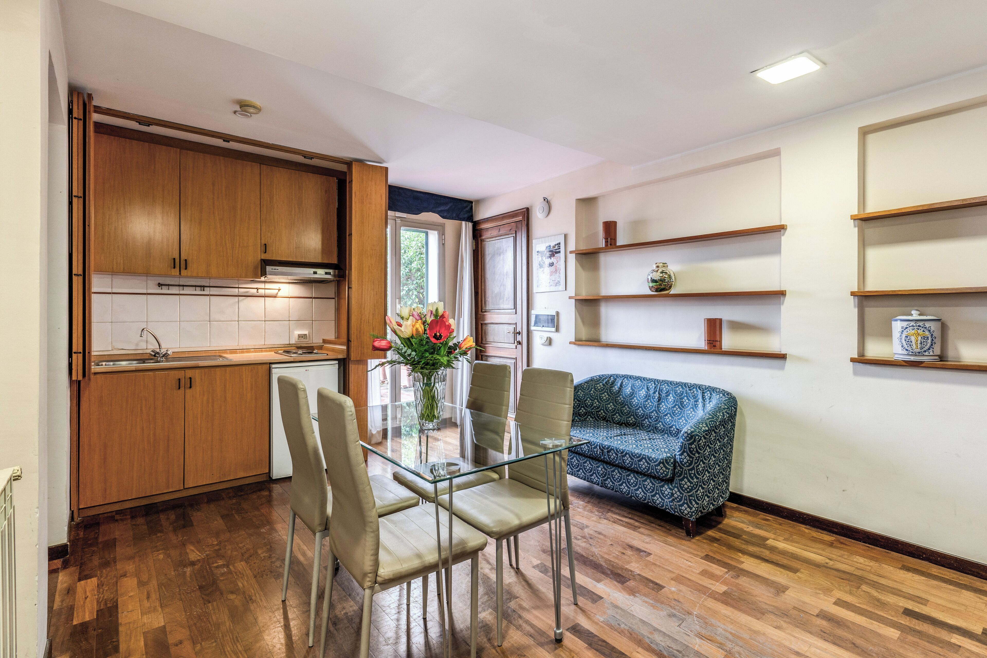 Cocina compacta con armarios de madera, una mesa de comedor con sillas y un sofá.