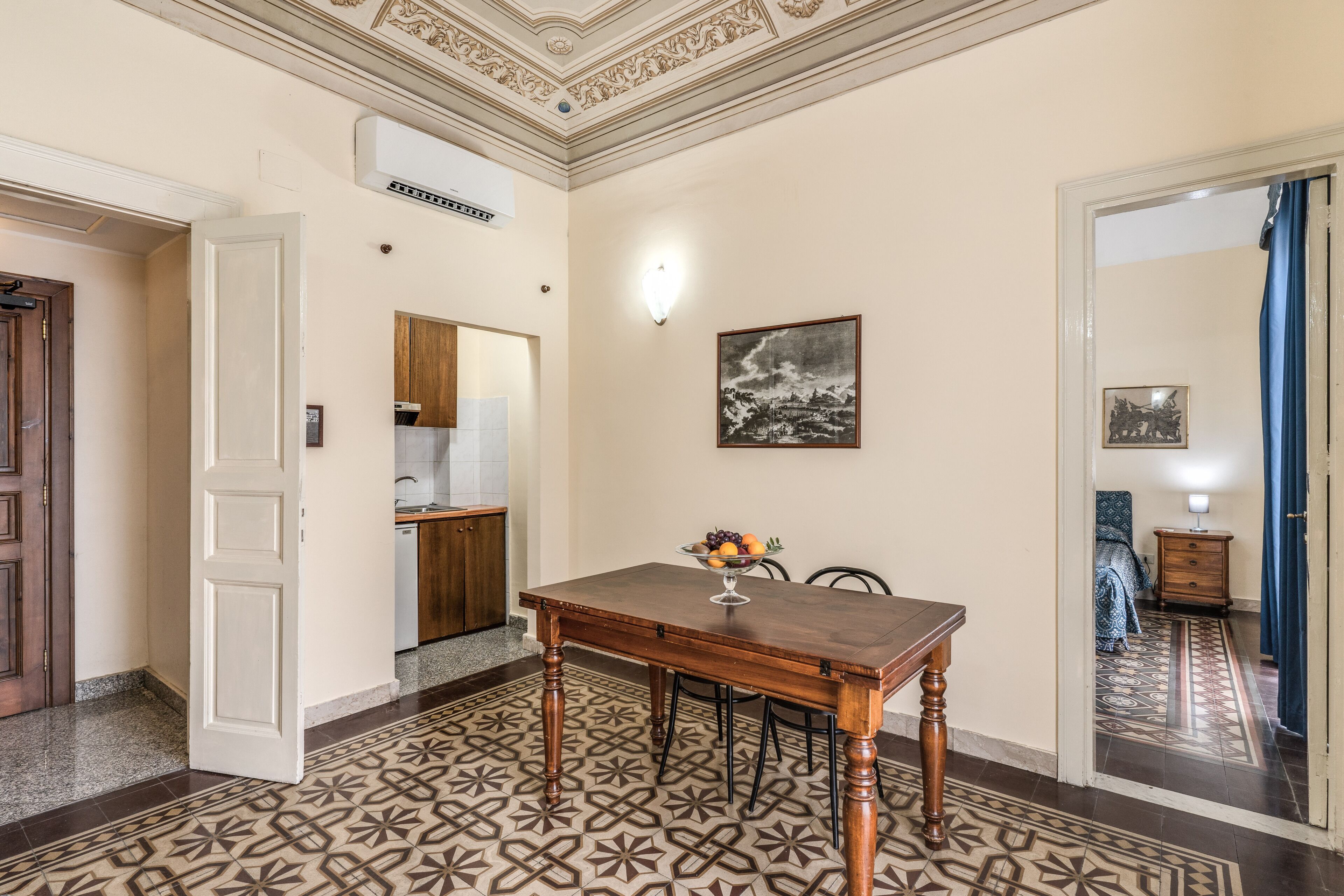A dining area with a wooden table and chairs, a patterned floor, and a ceiling with decorative molding.