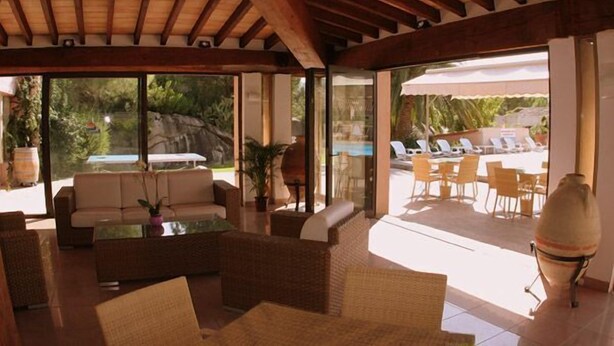 Amplo espaço interno com vista para piscina, móveis de vime e porta de vidro que dá para o exterior.