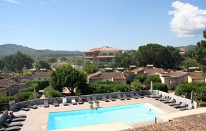 A pool area with lounge chairs, a swimming pool, and a view of surrounding buildings and hills.