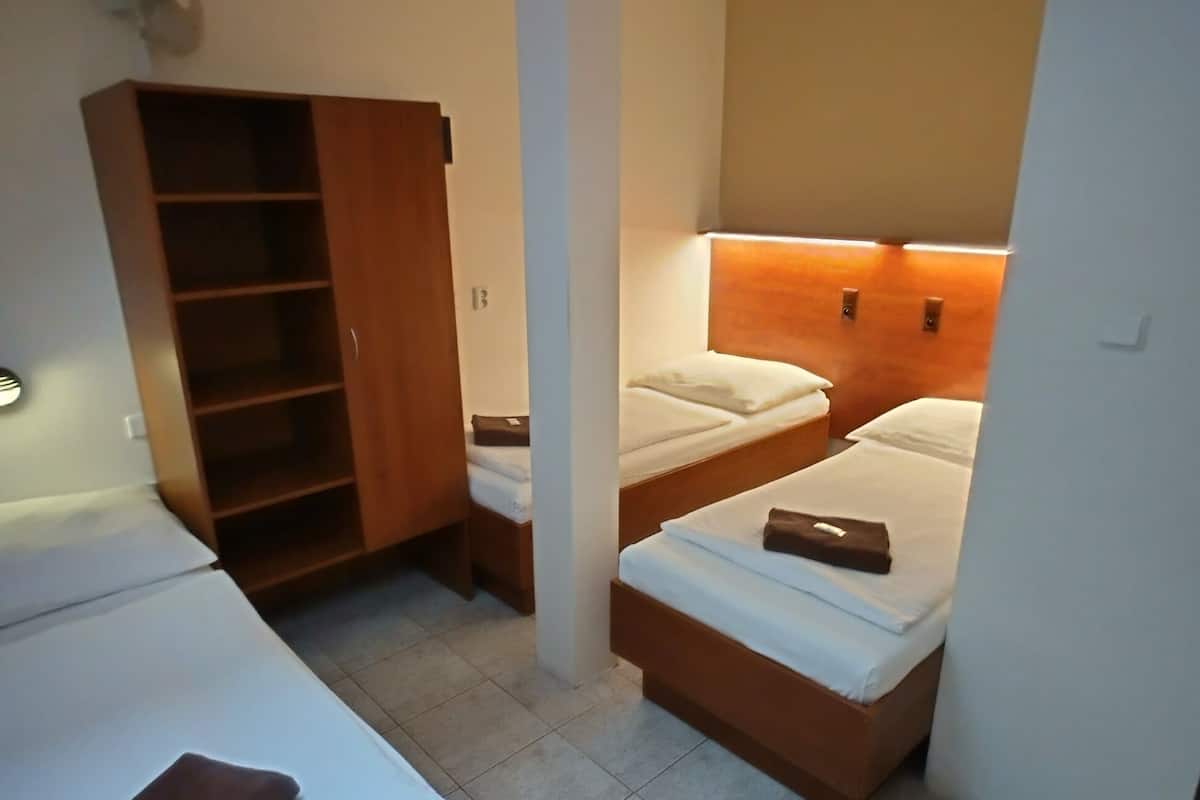Une chambre avec deux lits simples, une armoire en bois et une tête de lit dotée d’un éclairage intégré.