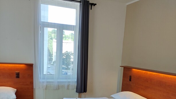 Ein Hotelzimmer mit zwei Betten, Holz-Kopfteilen, einem Fenster mit Vorhängen und einer Heizung.