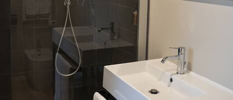 Un baño moderno con ducha envuelta en cristal, un lavamanos blanco y un espejo grande.