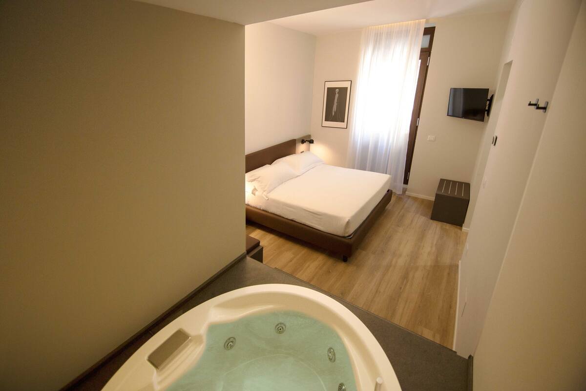Una habitación de hotel con una cama, un televisor montado en la pared y un baño con bañera.