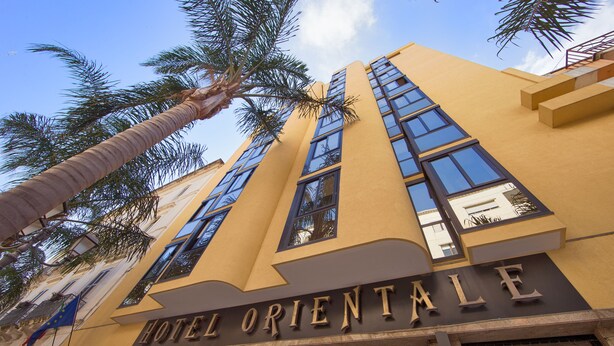 A hotel named "HOTEL ORIENTALE" with a modern facade, large windows, and palm trees in the foreground.